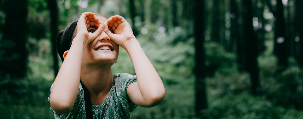 Child in a forest looking through hands as if they are binoculars