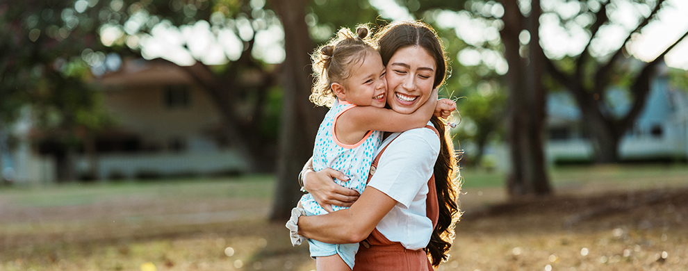 woman and girl smiling and hugging in a park